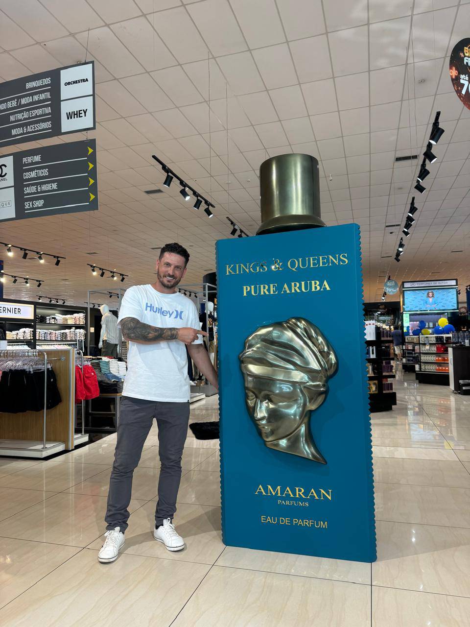 Homem ao lado de uma réplica cenográfica de frasco de perfume em grande escala